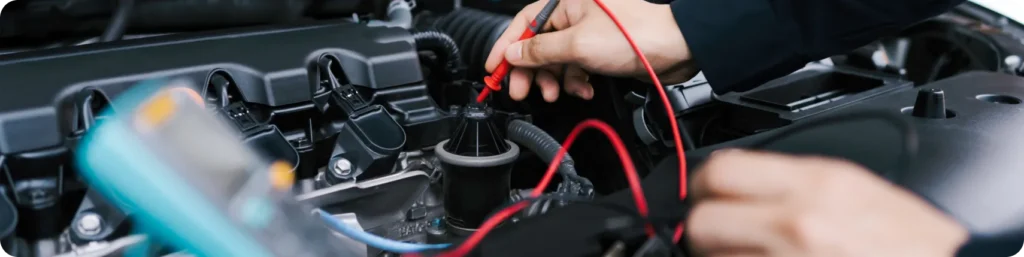 A close-up of a persons hands using red and black multimeter probes to test the engine components under a car hood. auto electrical repair, auto repair services in South Jordan UT