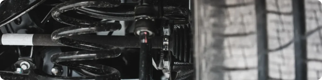 Close-up view of a car’s suspension system showing a coiled spring, shock absorber, and part of a tire, highlighting the vehicle’s undercarriage and mechanical components. Steering and Suspension Repair, auto repair services in South Jordan UT