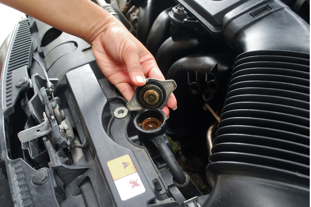 Cooling system maintenance in South Jordan, UT by Performance Place. Image of a person opening a radiator cap to inspect the coolant reservoir under the hood.