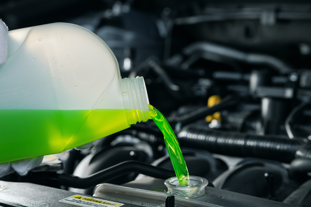 Antifreeze Protects Your Engine in South Jordan, UT by Performance Place. A person pouring green antifreeze into a car's engine, illustrating the process of maintaining engine health during winter.